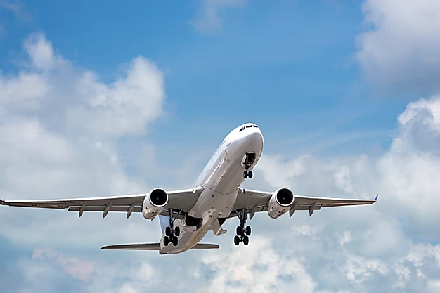 Commercial passenger airplane flying with landing gear deployed beneath a blue sky with scattered clouds for performing umrah.