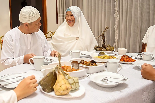 Happy Muslim family enjoying a traditional meal together with halal dishes and ketupat during Hajj and Umrah Pilgrimage