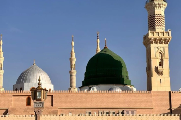 Green Dome and white domes of Masjid-e-Nabawi with a towering minaret in Madinah.