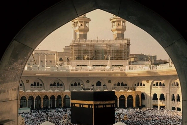 Kaaba viewed through a stone archway with pilgrims and two minarets at Masjid al-Haram in Makkah.