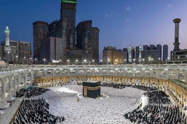 Evening view of the Kaaba with pilgrims offering Salah and the Abraj Al Bait Clock Towers in Makkah.