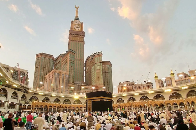 Holy Kaaba at Masjid-al-Haram with the Makkah Clock Tower in the background and pilgrims gathered for worship in Makkah, Saudi Arabia.