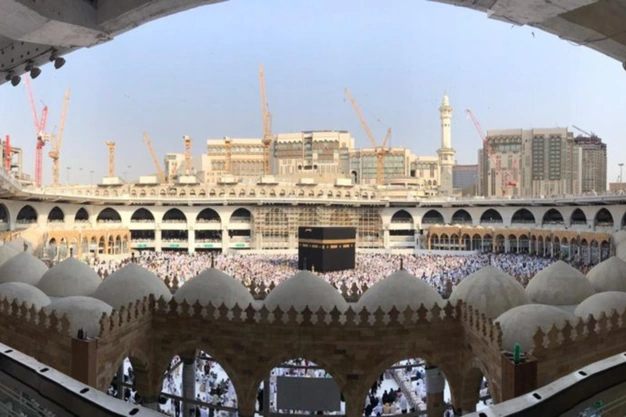 Framed view of the Kaaba at Masjid-al-Haram with pilgrims, arches and surrounding buildings in Makkah.