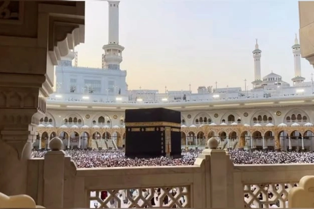 View of the Kaaba in Makkah framed by an ornate balcony, pilgrims for Tawaf