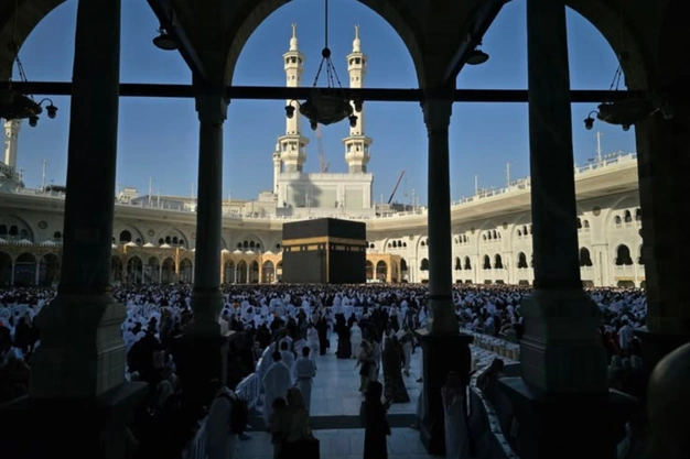 Framed view of the Kaaba with two minarets and pilgrims at Masjid al Haram in Makkah.
