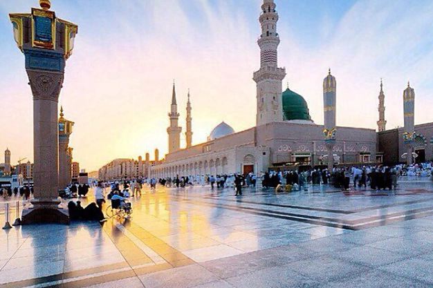 Sunset view of the courtyard of Masjid-e-Nabawi with the Green Dome, minarets and worshippers in Madinah.