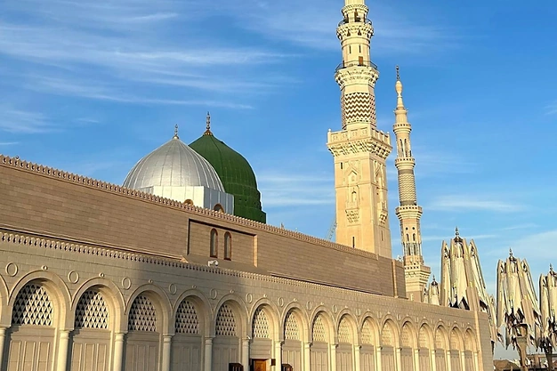 Close-up view of Al Masjid-an-Nabawi with Green Dome adjacent silver dome, ornate mosque arches and towering minarets under blue sky