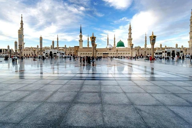 Wide view of the courtyard of Masjid-e-Nabawi with the Green Dome and minarets beneath a blue sky in Madinah.