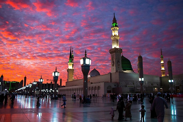 Masjid-e-Nabawi with the Green Dome and illuminated minarets beneath a vibrant sunset sky in Madinah.