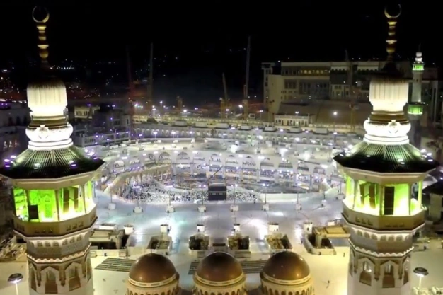 Night view of the Holy Kaaba in Makkah with illuminated minarets and Muslim pilgrims performing Tawaf during Umrah