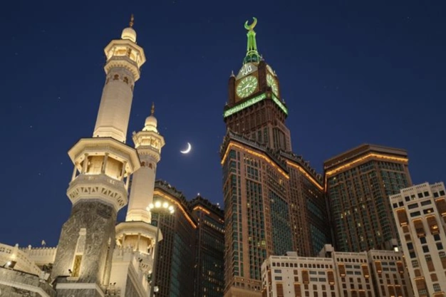 Night view of the Abraj Al Bait Clock Tower and Haram minarets beneath a crescent moon in Makkah