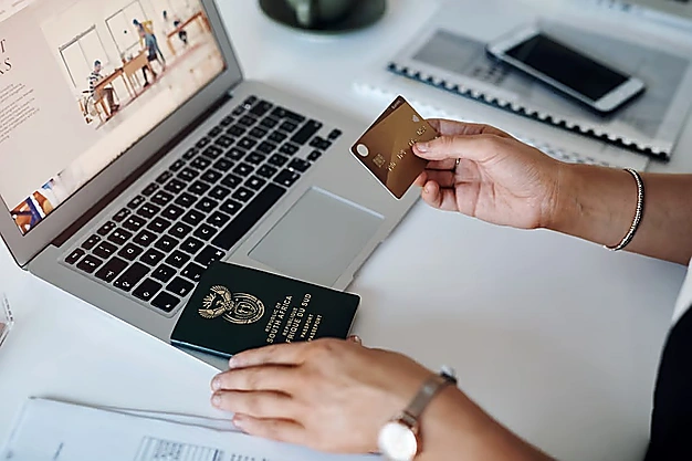 Person holding a credit card while booking travel online with a laptop and passport, representing online Umrah
