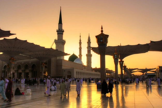 View of The Prophet's Mosque at sunset with the Green Dome, towering minarets, open courtyard umbrellas, and Muslim worshippers